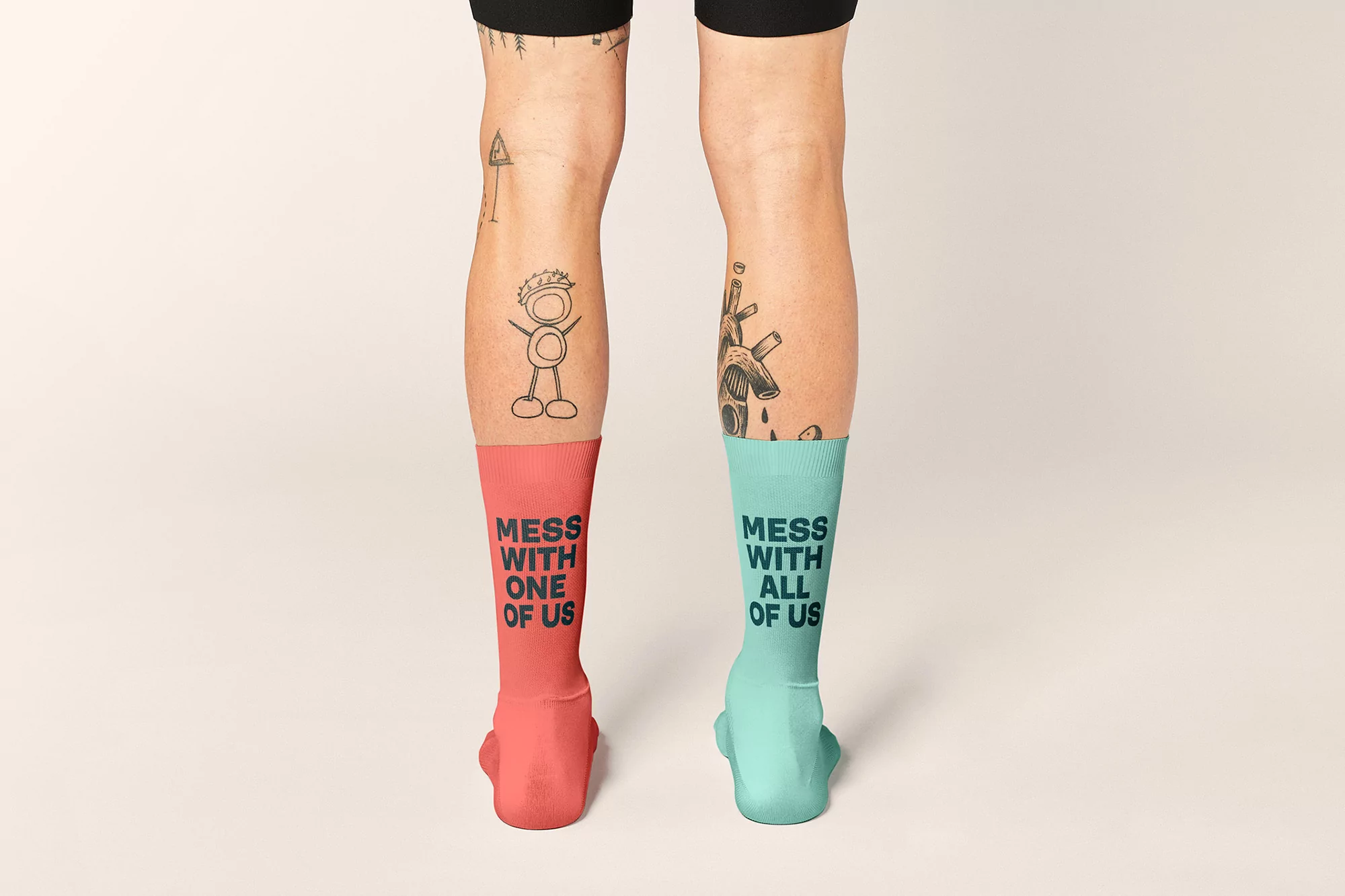Two human legs wearing mismatched colorful socks, standing against a white background, featuring text and tattoos on the legs.