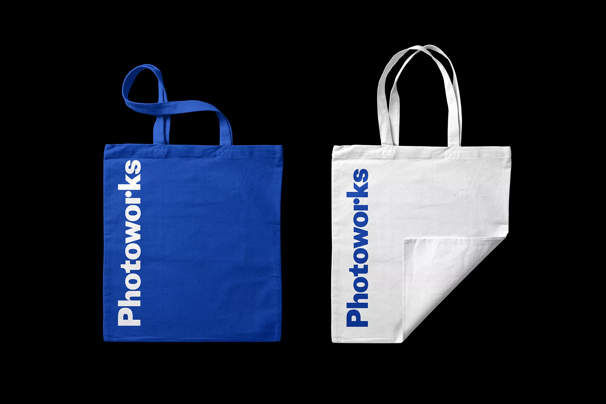 Two tote bags on a black backdrop: a blue one on the left with white text and a white one on the right with blue text.