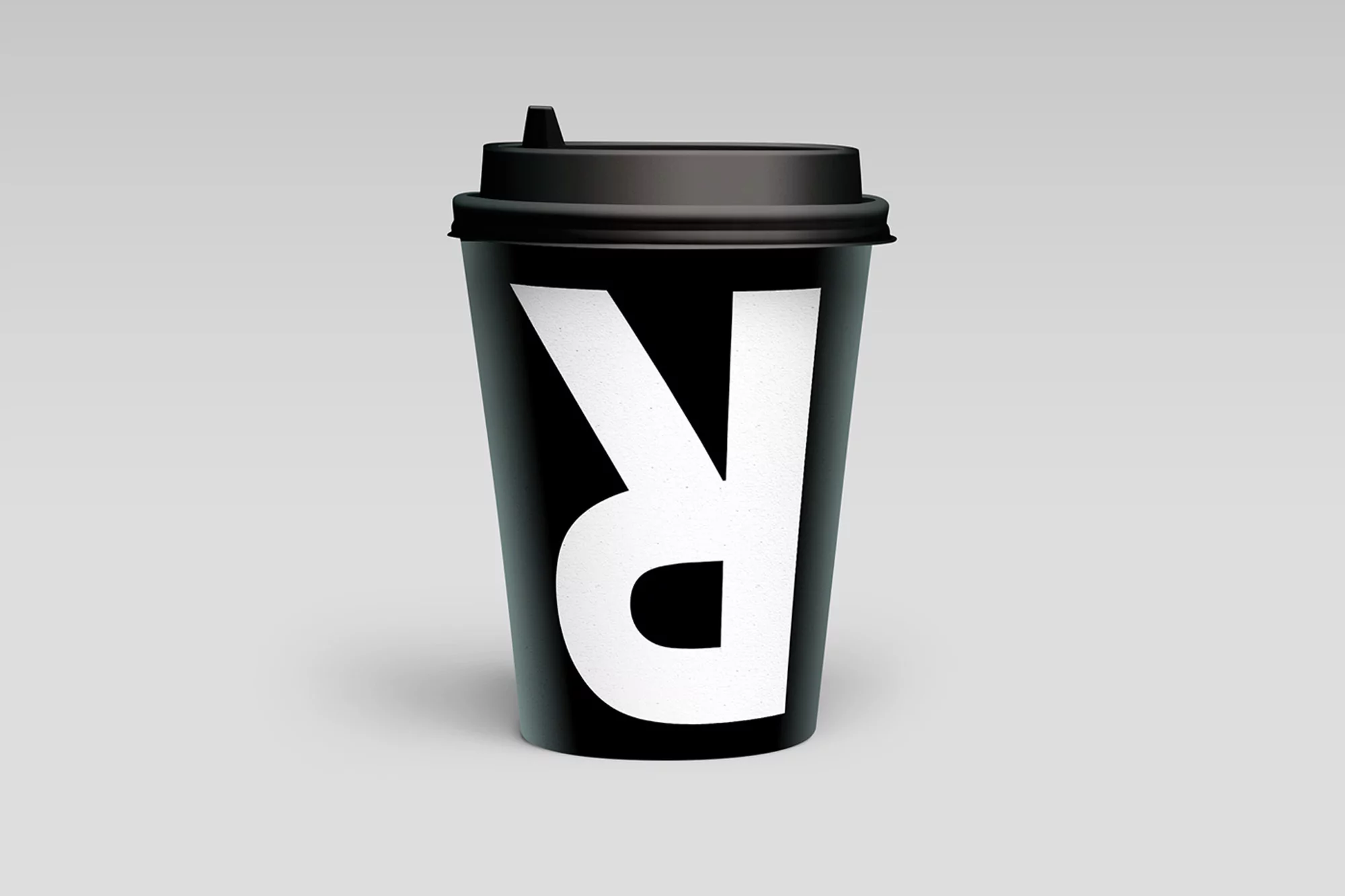 Studio shot of a black coffee cup with a white letter R logo on a gray background. Simple product shot for commercial use.