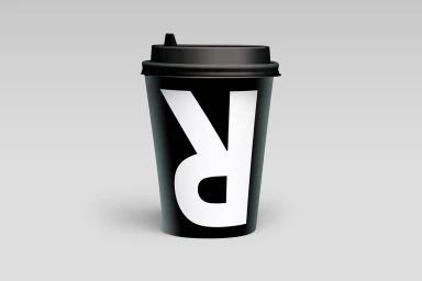 A black takeaway coffee cup with a white letter branding against a seamless grey studio background.