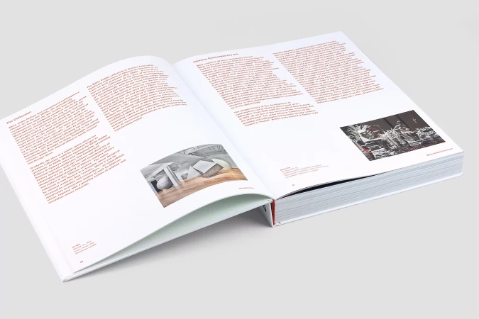 Open book displays art and text on white pages with color pictures. Book has a red spine and gray background.