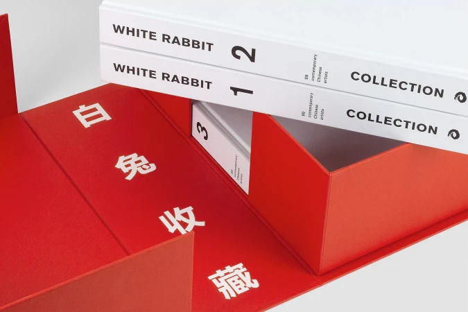 Three White Rabbit Collection art books are stacked in a red box with Chinese characters on a white background in a studio setting.