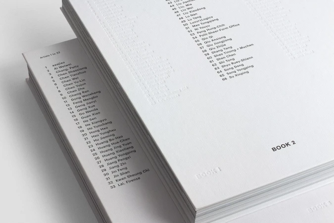 Two open books display lists of artist names and numbers in a white on white aesthetic, showing minimalistic design and information.