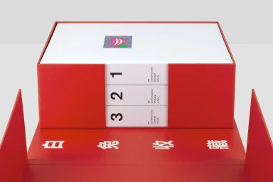 Red presentation box housing three white books labeled 3, 2, and 1 against a white studio background.