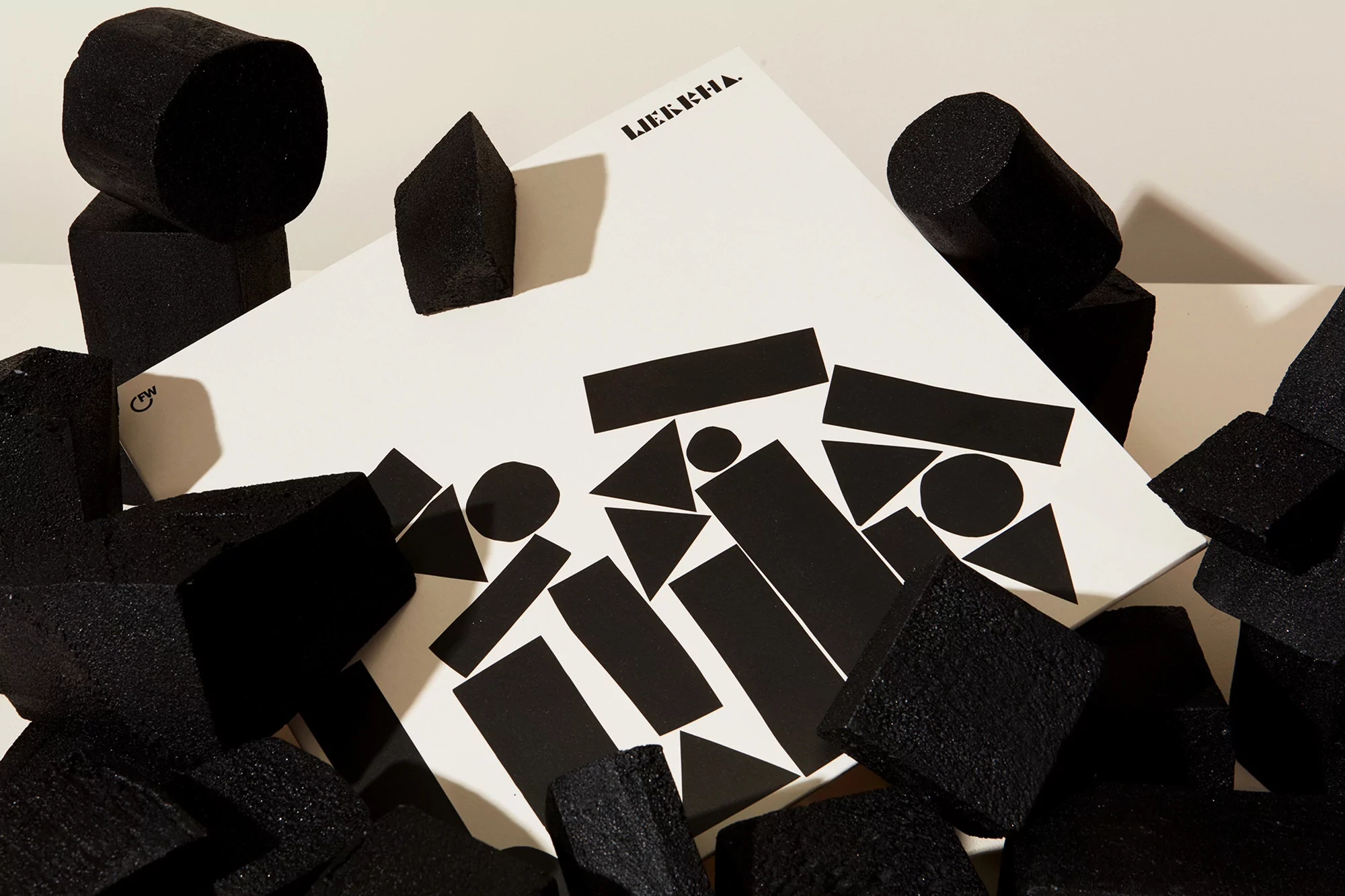 Abstract shot of black geometric foam blocks around a white board with black geometric shapes against a cream colored background.