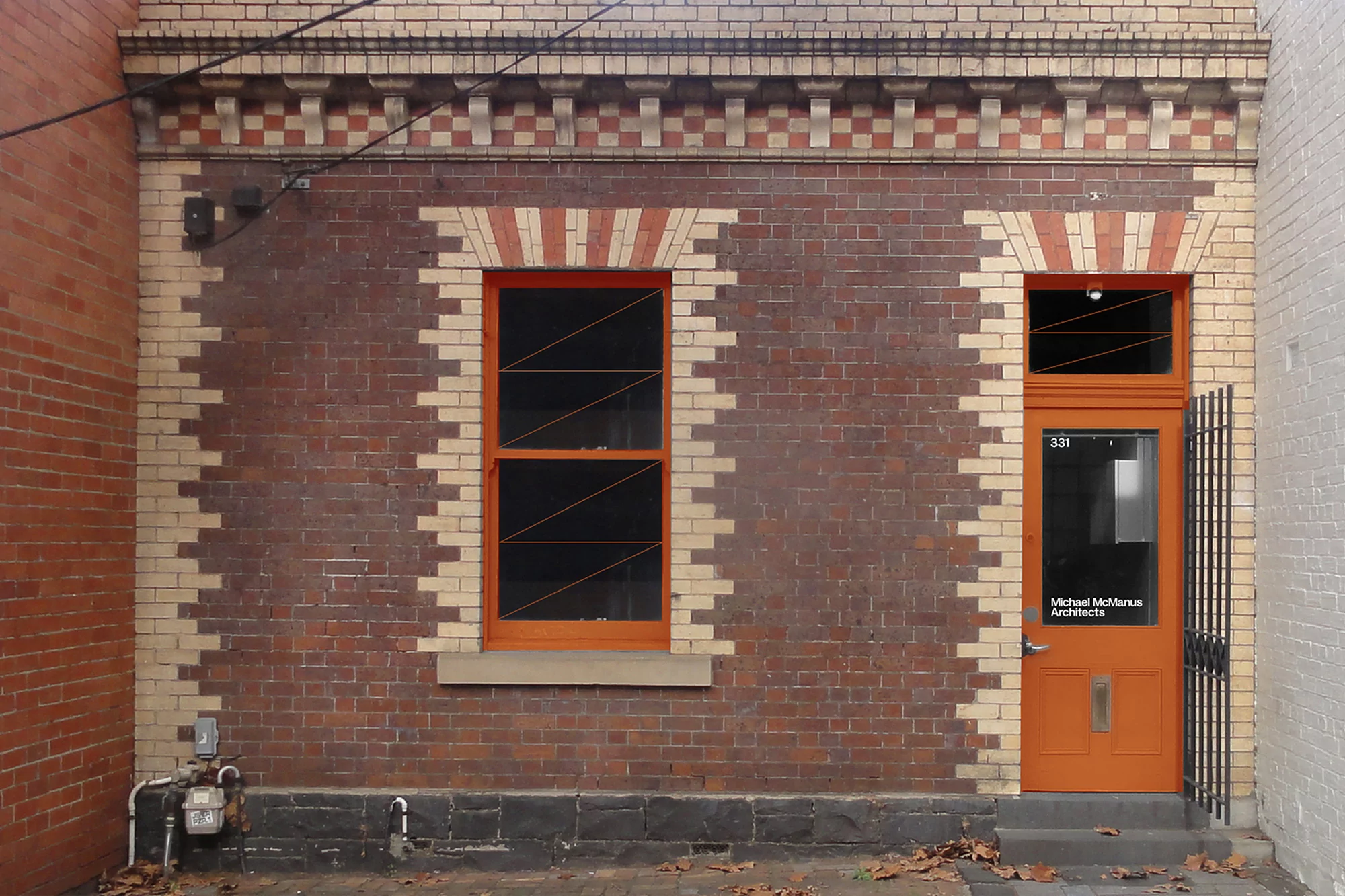 Exterior of a brick building with an orange door and window frames, showcasing architectural details and urban design.