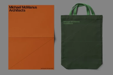 An orange document featuring black typography alongside a dark green fabric tote bag on a grey background