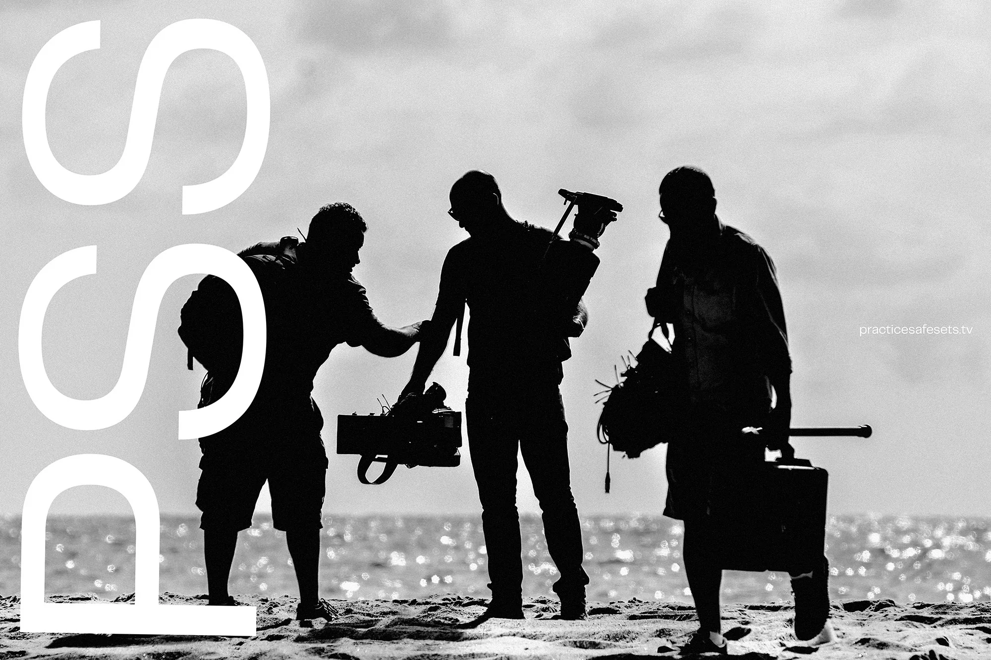 Three silhouetted videographers on a beach at daytime, holding cameras and equipment, stand against a bright sky and glittering water.