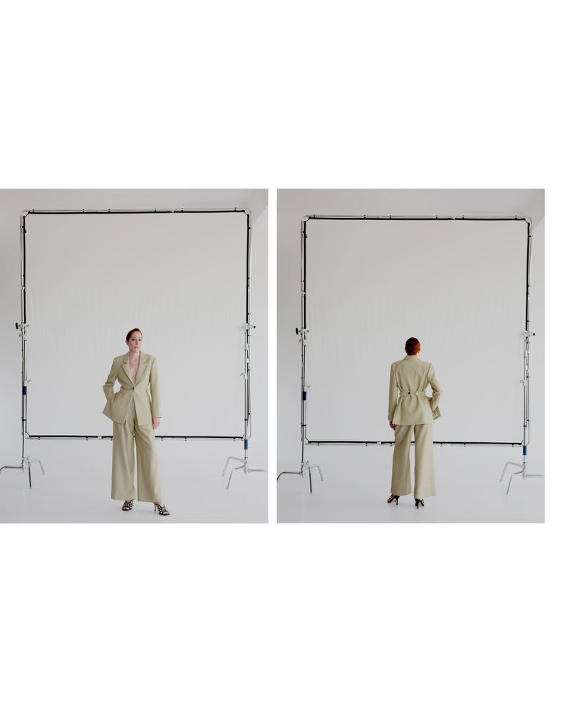 Front and back views of a female fashion model wearing a light tan suit in a studio setting, standing in front of white screens.