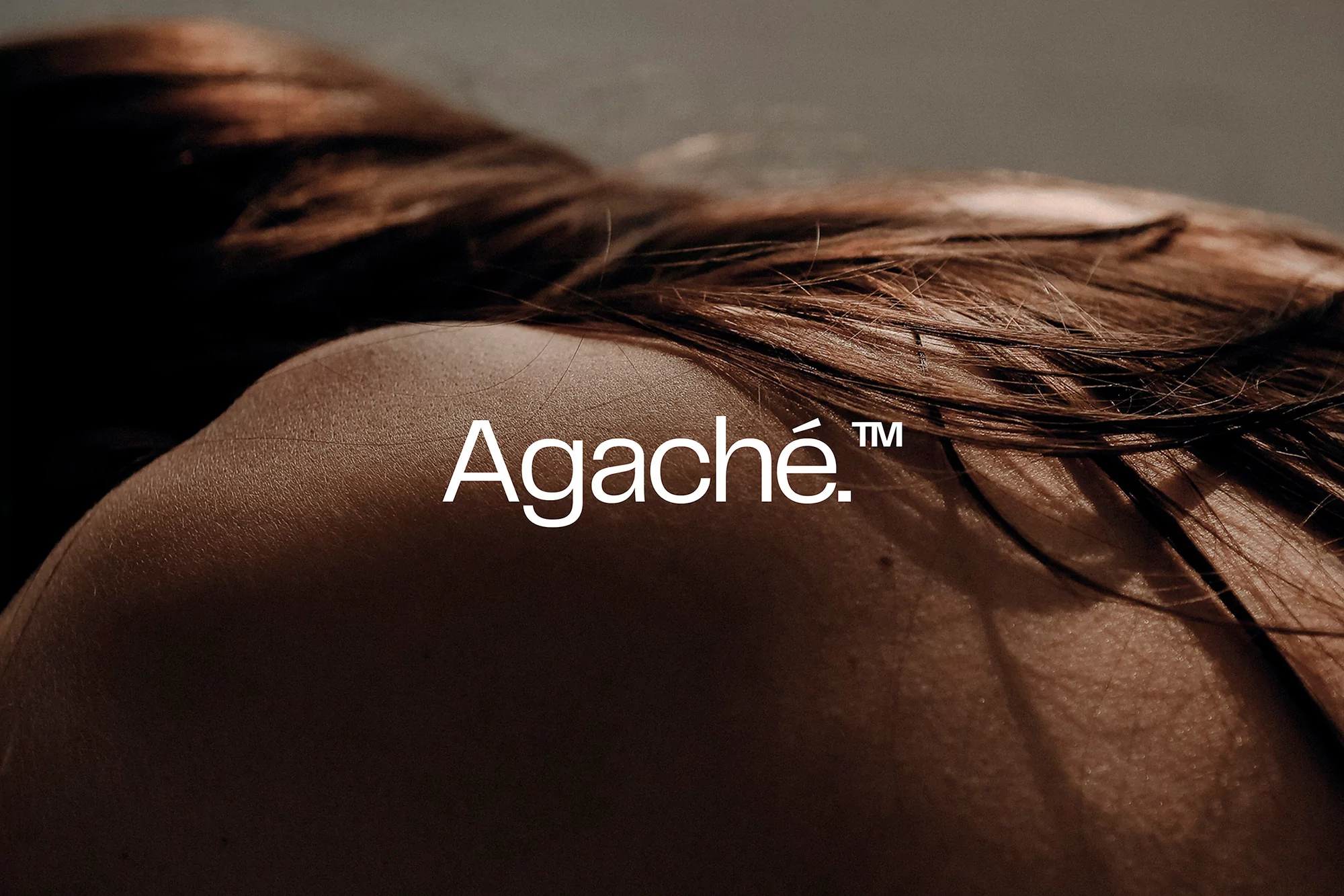 Close-up studio shot of a brunette adult female lying down with her back visible.  Fashion and beauty photography with logo overlay.