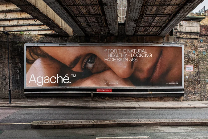 Close-up beauty ad billboard with tan skin, featuring the brand name Agache, set against an urban street and weathered underpass.