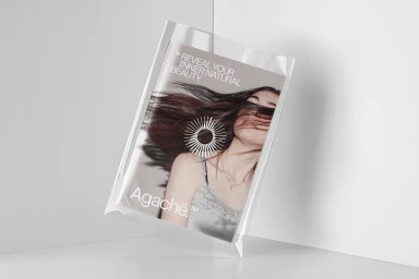 Printed booklet inside a clear plastic packaging bag featuring a woman with hair across her face and the Agaché brand logo.
