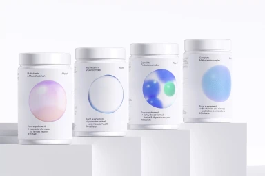 Four white supplement bottles with colorful circular graphic labels arranged on tiered white display blocks.