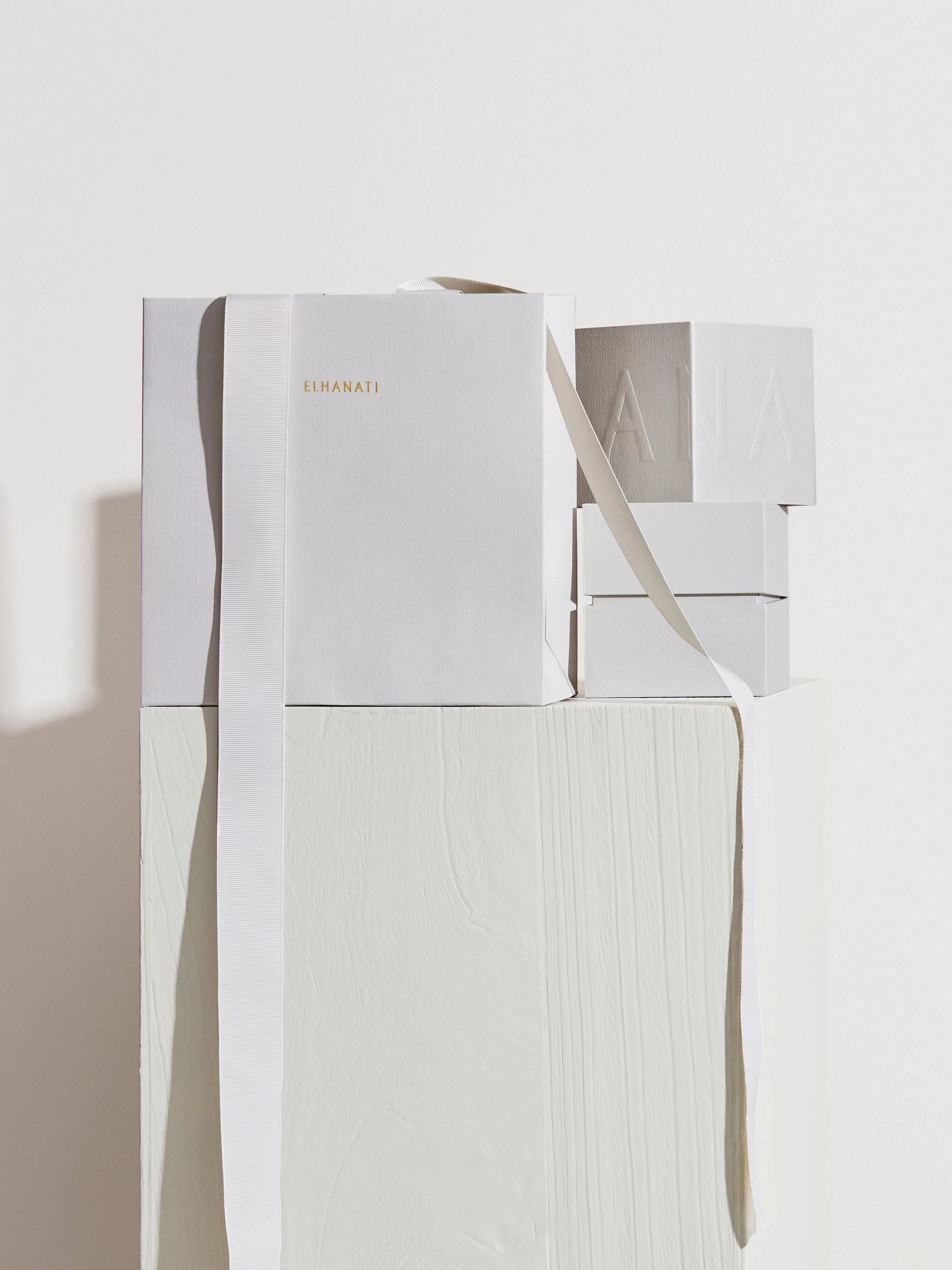 Stacked white gift boxes with ribbons on a painted white wooden surface in a brightly lit studio setting.