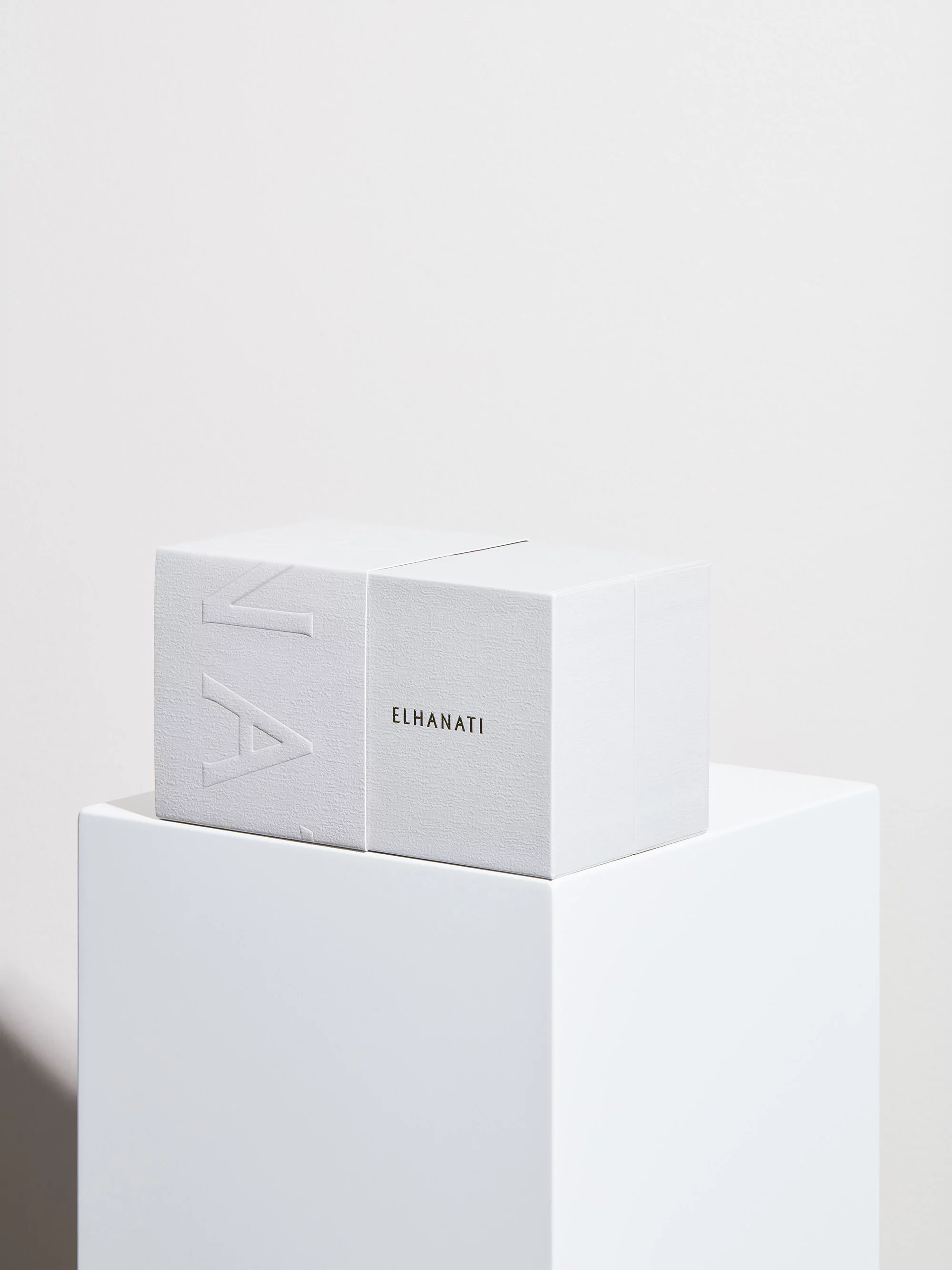 White ELHANATI gift box with embossed lettering resting on a white display pedestal against a neutral background