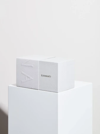 White ELHANATI gift box with embossed lettering resting on a white display pedestal against a neutral background