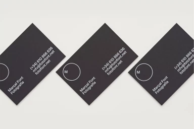 Three dark rectangular business cards arranged diagonally on a neutral off-white surface featuring minimalist white typography.