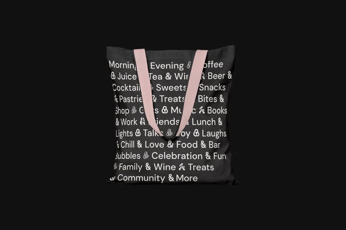 Black tote bag with pink handles and text graphics on a black background. Stylish, reusable bag for shopping and everyday use.