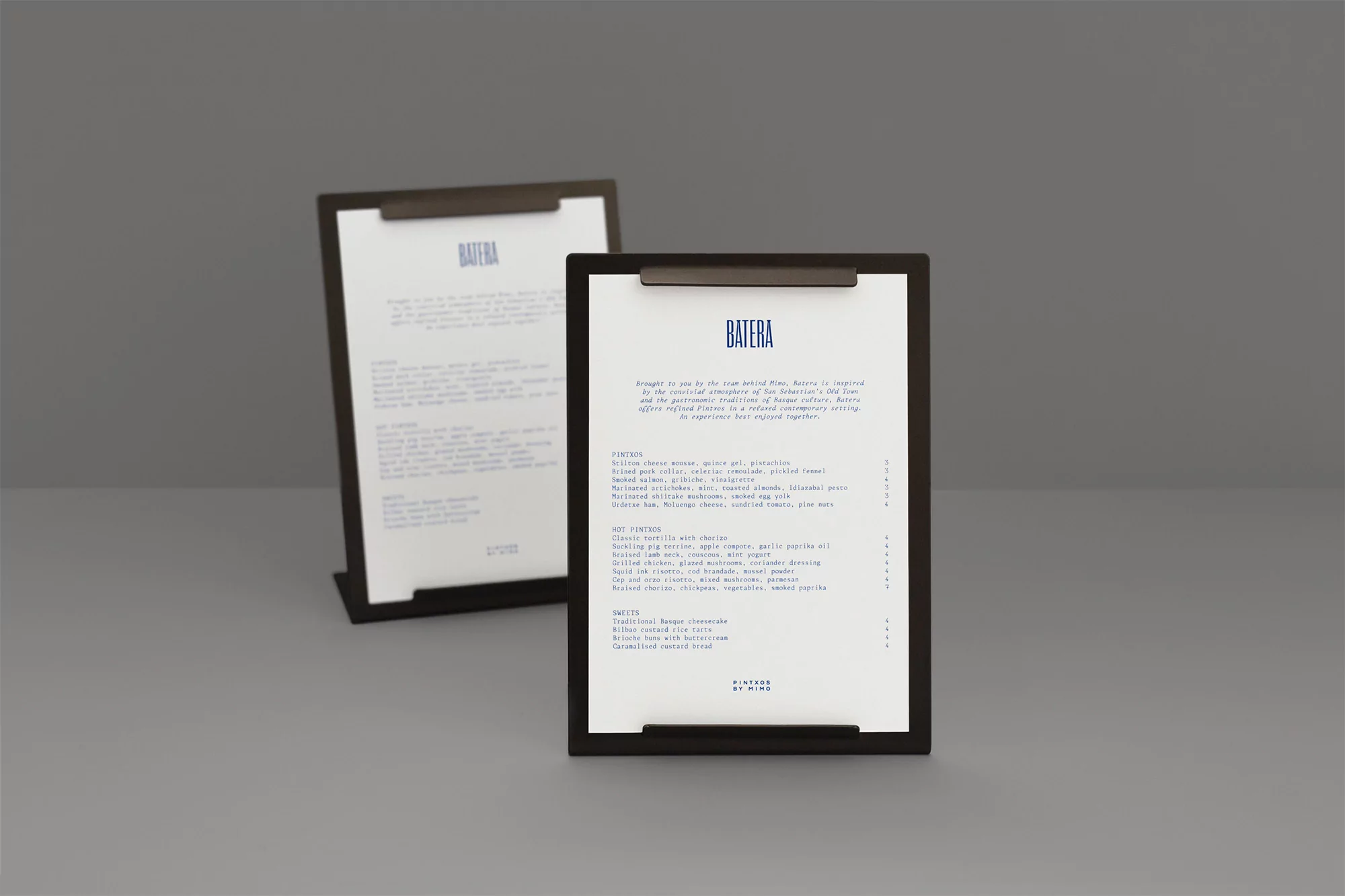 Two framed Batera restaurant menus present menu items and descriptions in blue text on white paper in a minimalistic composition.