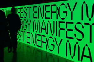 Silhouette of a person walking past a large glowing neon green display wall with repeating typographic lettering
