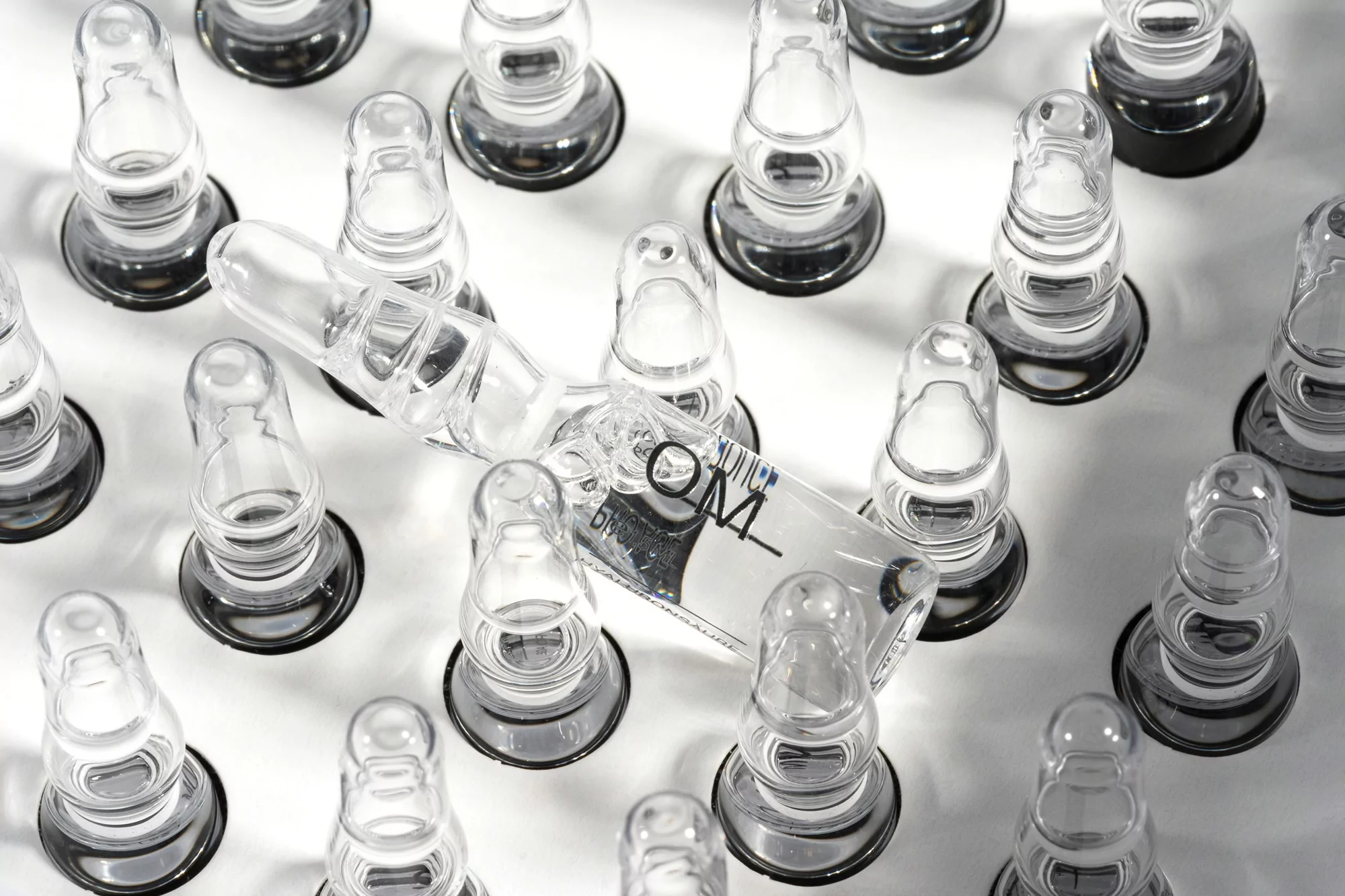 Close-up of clear glass ampoules on a white surface, showcasing pharmaceutical or cosmetic vials arranged in a structured pattern.