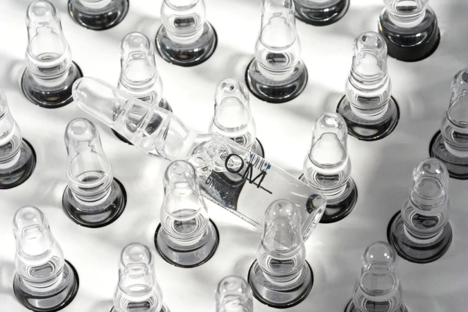 Close-up of clear glass ampoules on a white surface, showcasing pharmaceutical or cosmetic vials arranged in a structured pattern.