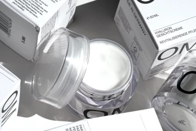Open OM face cream jar surrounded by matching white product packaging boxes under clean light