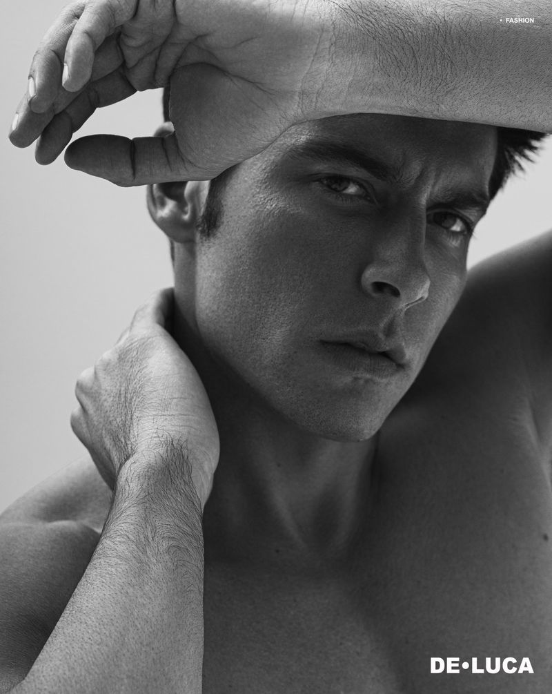 Striking black and white portrait of a man with hand raised to head, capturing intense gaze and upper body in a simple setting.