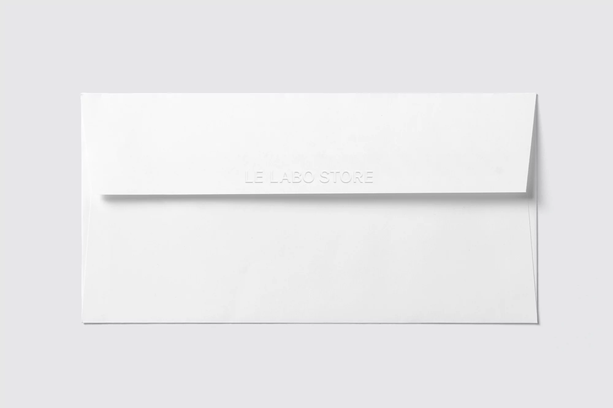 Studio product shot of a white envelope with 'LE LABO STORE' embossed, presented on a light gray background, minimalist and clean aesthetic.