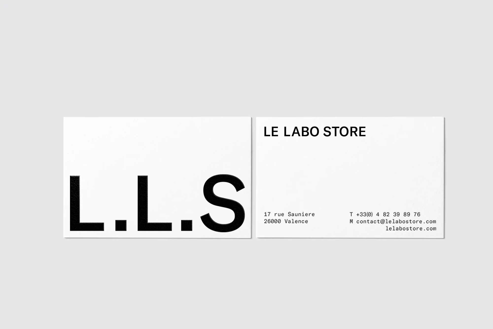 Two white business cards with black text are displayed on a light grey surface, one featuring the company name and address.