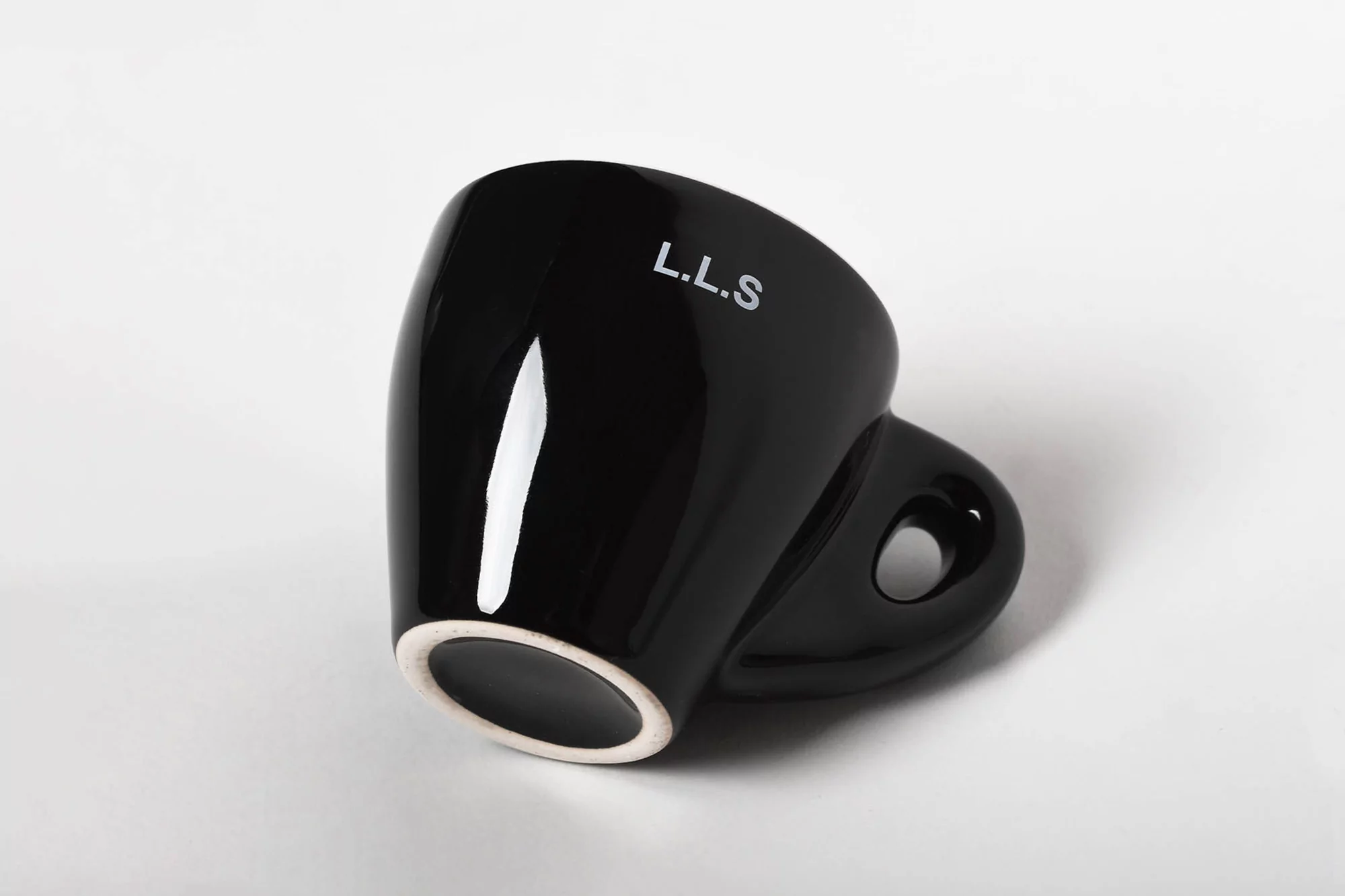 Close-up studio shot of a glossy black ceramic coffee mug with the letters L.L.S. against a plain white background.