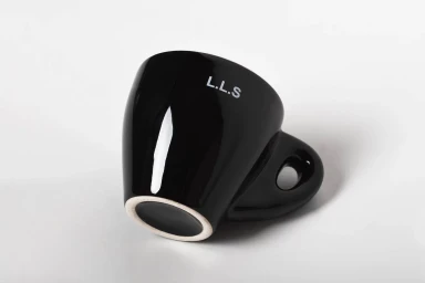 Black ceramic espresso cup tilted on a white seamless background with white text printed on the side