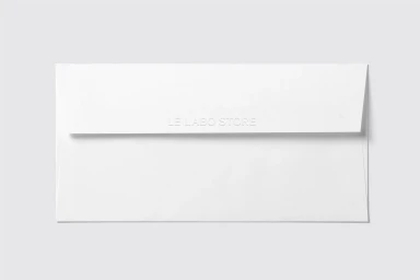 White paper envelope with embossed lettering centered on a plain light grey studio backdrop