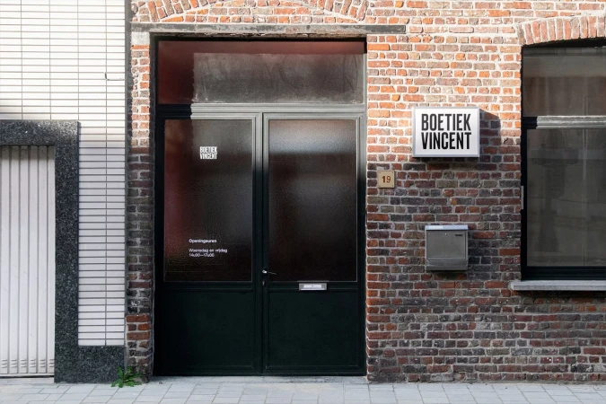 Exterior view of 'Boetiek Vincent' storefront, featuring a dark green door, brick facade, address number '19', and window.