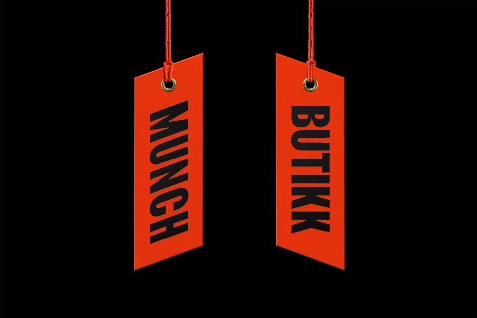 Two vibrant orange tags hang against a stark black background, each labeled 'MUNCH' and 'BUTIKK' in bold, sans-serif black text.