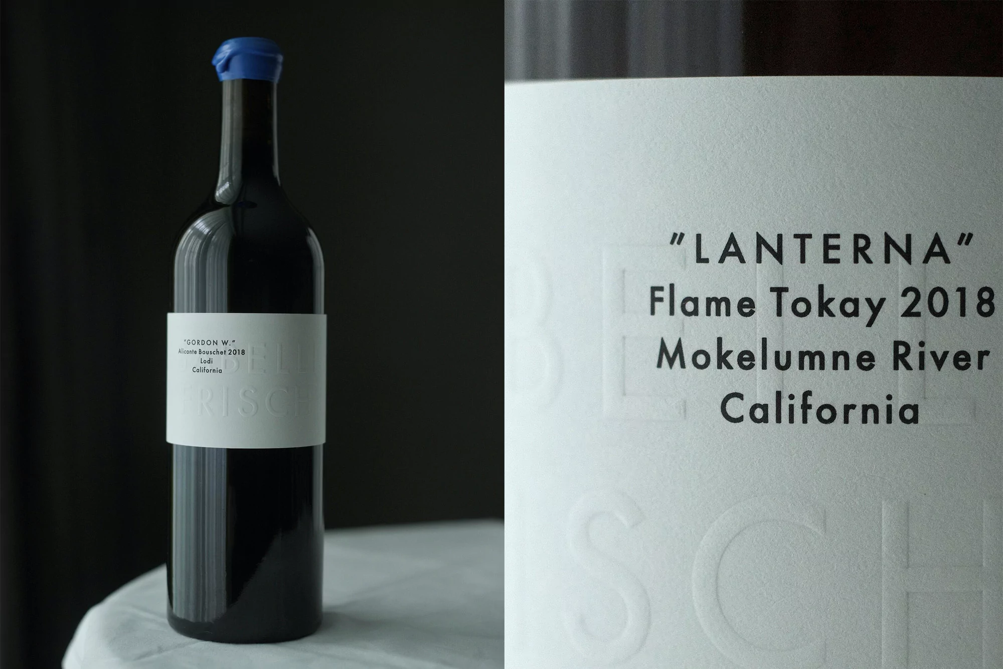 A bottle of red wine with a blue cap sits on a white tablecloth against a dark background, featuring a white label with black text.