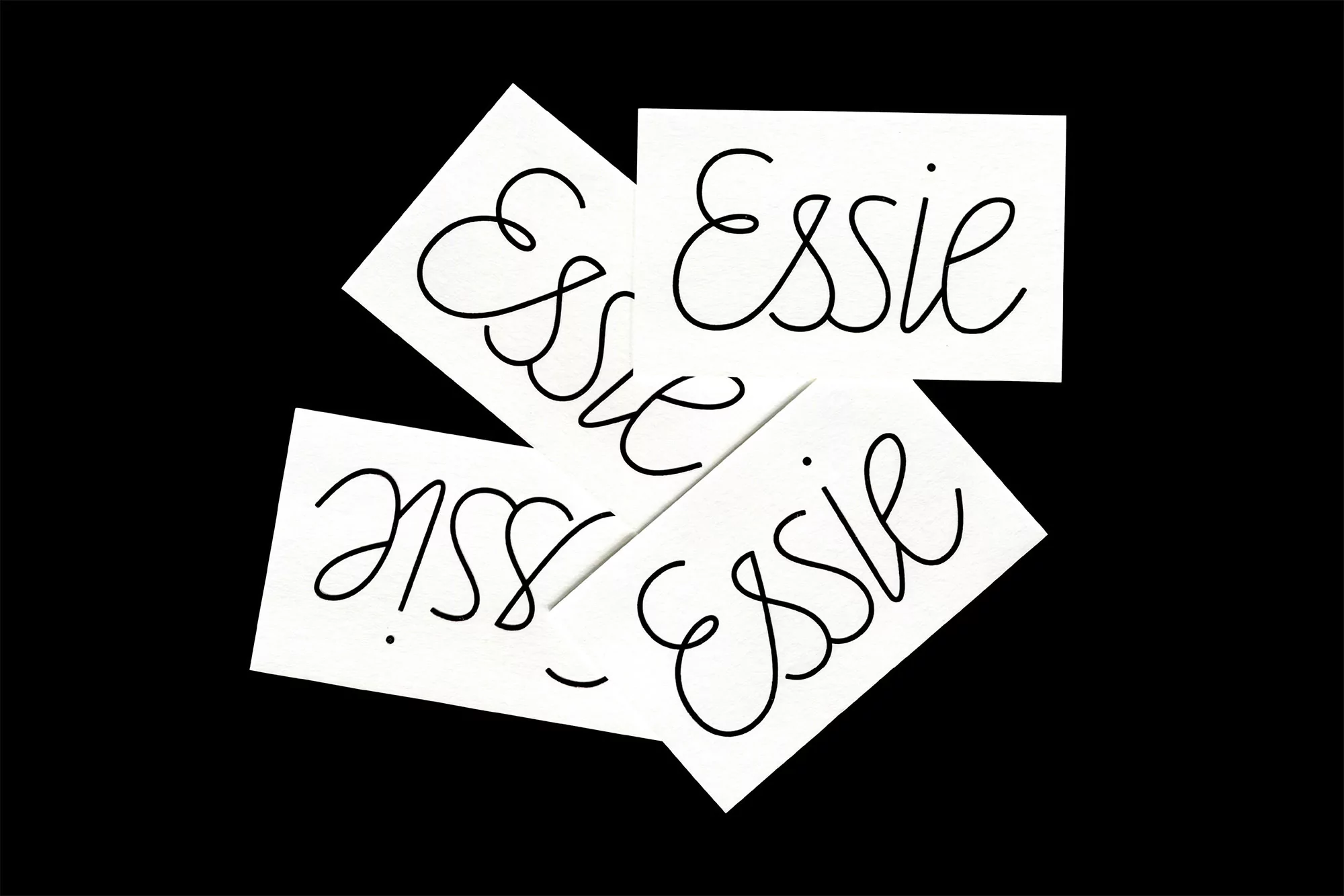 Multiple white cards with the word 'Essie' in black cursive font are arranged against a stark black background in a studio setting.
