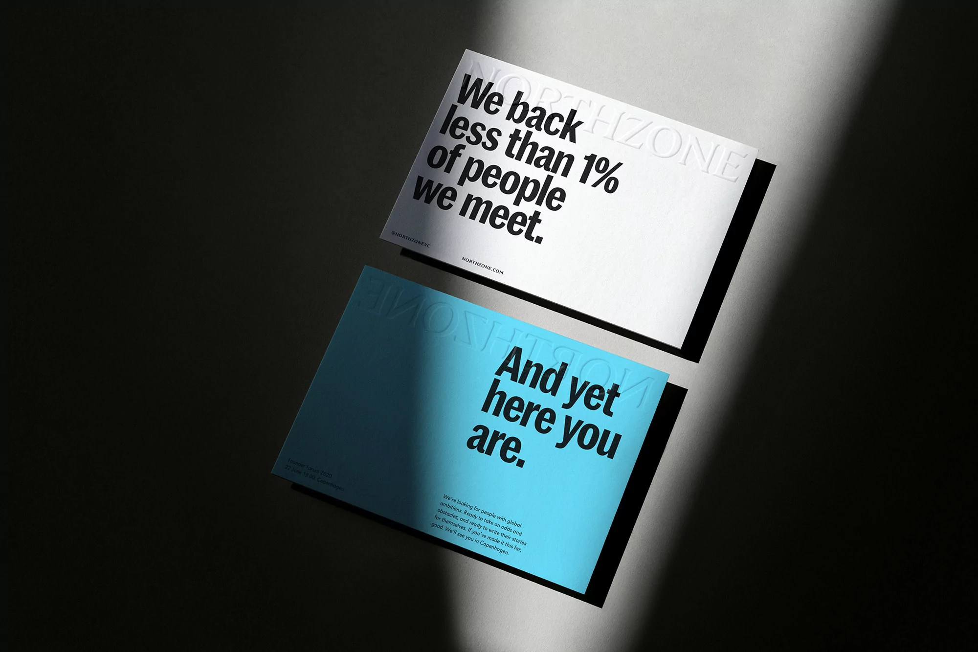Two promotional cards, one white and one light blue, angled on a gray surface with a ray of light illuminating them.