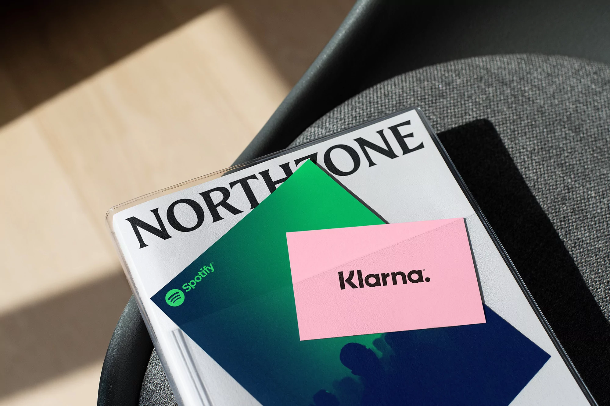 A magazine with the brand names Northzone, Spotify, and Klarna displayed on top of a grey fabric chair indoors.