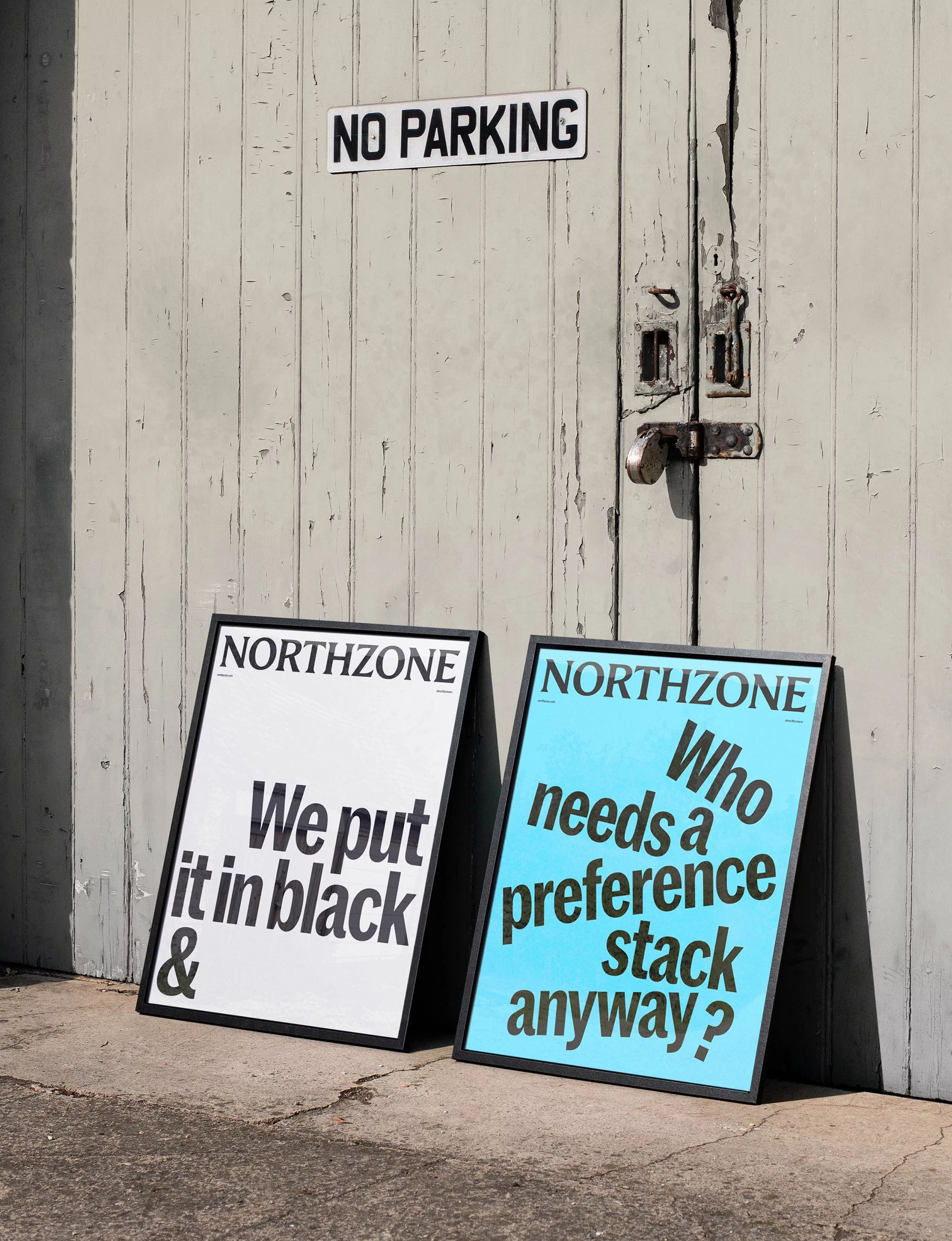 Two framed Northzone posters with contrasting designs stand outdoors against a weathered wooden door, a no parking sign above.