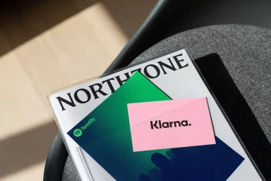 Close-up high angle shot of a Northzone branded publication featuring Spotify and Klarna graphic inserts resting on a textured dark chair