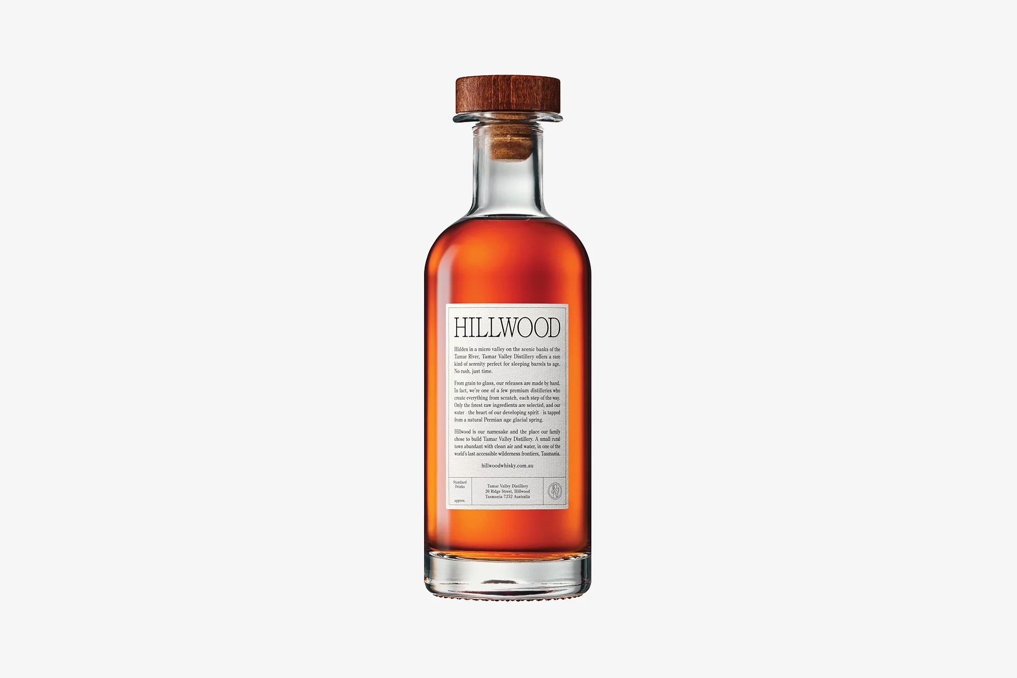 Hillwood bottle of liquor against white background. Brown liquid, clear glass, with wood stopper. Label with text description.