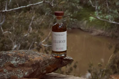 Hillwood whisky bottle resting on a mossy rock outdoors near a river and trees