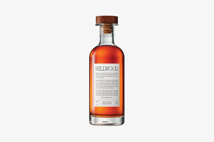 Glass bottle of Hillwood spirit with an amber liquid and a wooden cork stopper set against a white background