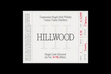 Close-up of a white paper product label for Hillwood Tasmanian Single Malt Whisky with black typography and handwritten red ink notations.