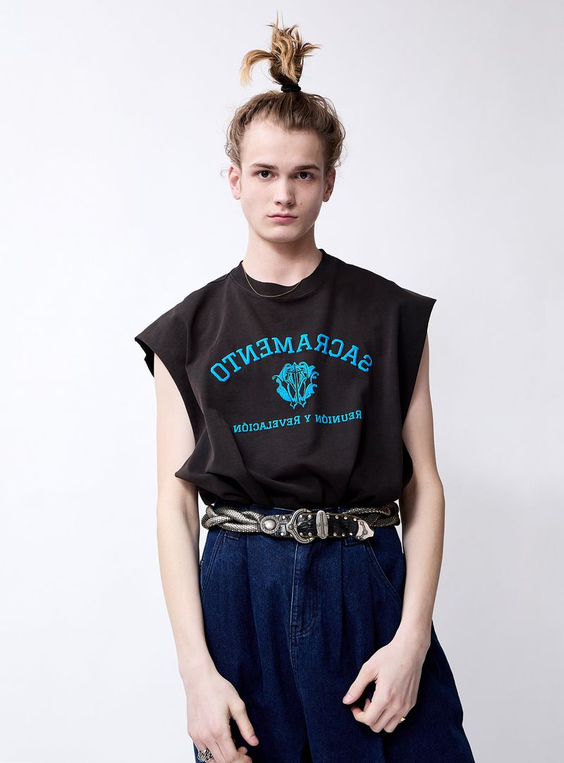 Studio portrait of a young adult male wearing a dark t-shirt with an inscription and wide-legged denim pants with a decorative belt.