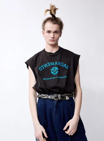 Studio portrait of a young adult male wearing a dark t-shirt with an inscription and wide-legged denim pants with a decorative belt.