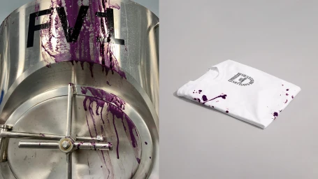 Stainless steel industrial tank with purple liquid drips alongside a neatly folded white t-shirt featuring dark graphics