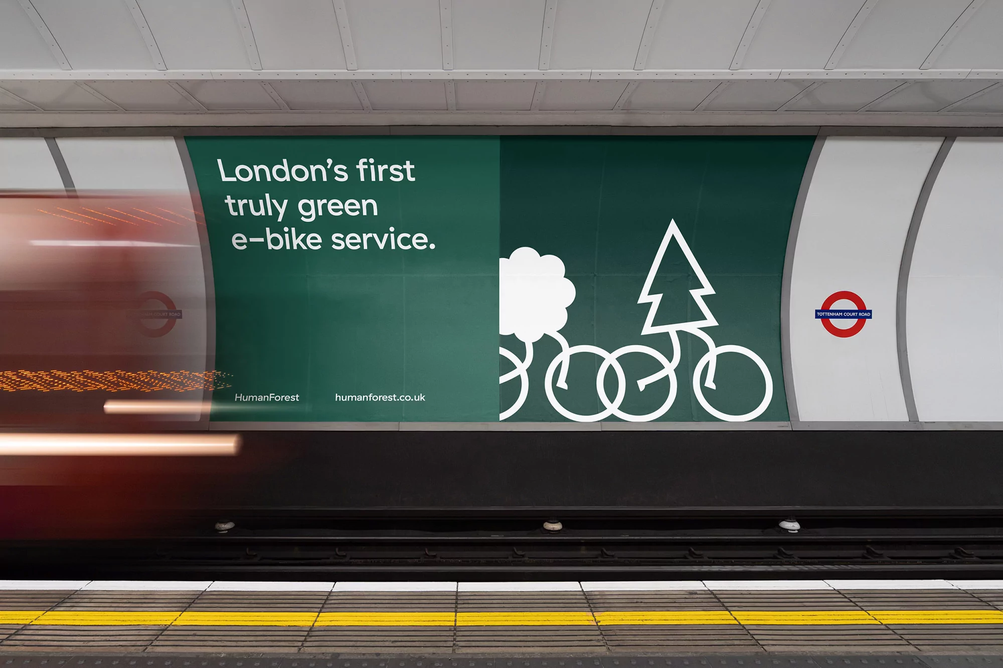 London underground advertisement features green e-bike service, tree and cloud icon linking to HumanForest website, moving subway train.