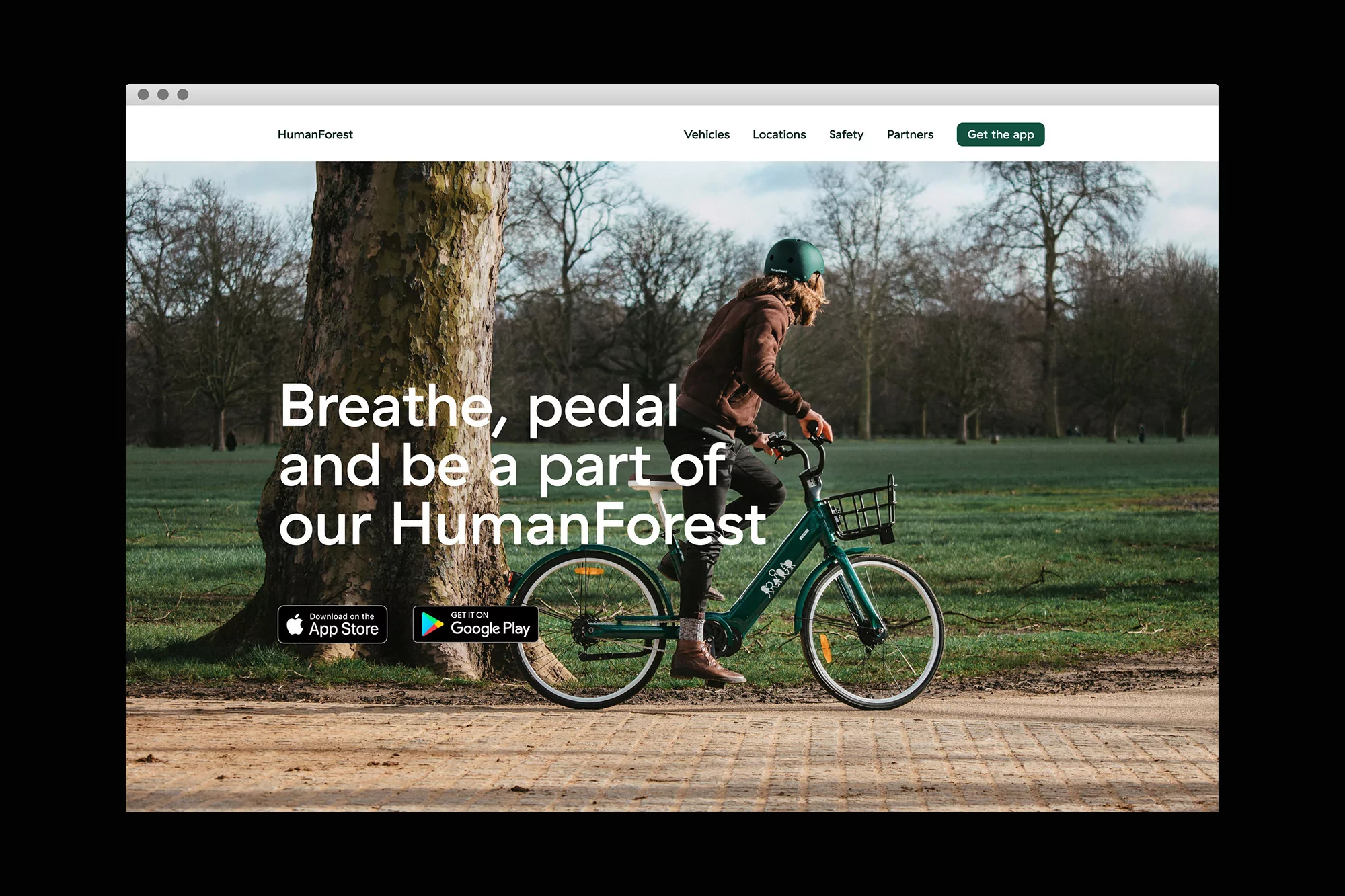 A person rides a bicycle on a path in a park on a HumanForest app landing page viewed on a monitor. The background is lush and green.